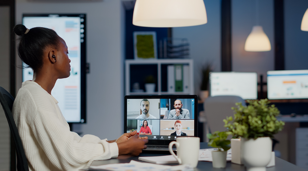 A black woman sits at her office desk, facing her computer screen engaged in a Zoom meeting with four coworkers.