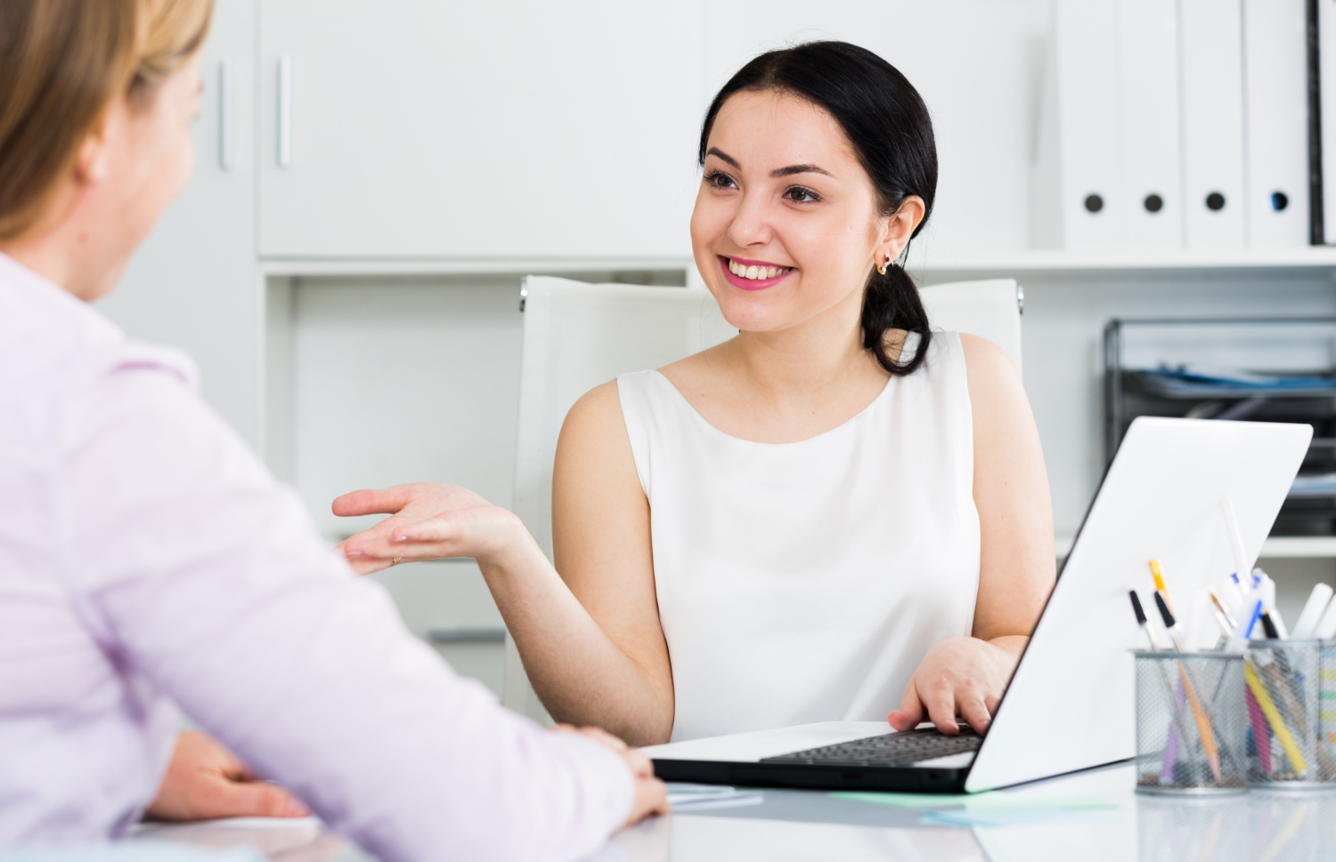 A female HR professional discussing with an applicant, holding a job application form in her hand during an interview.
