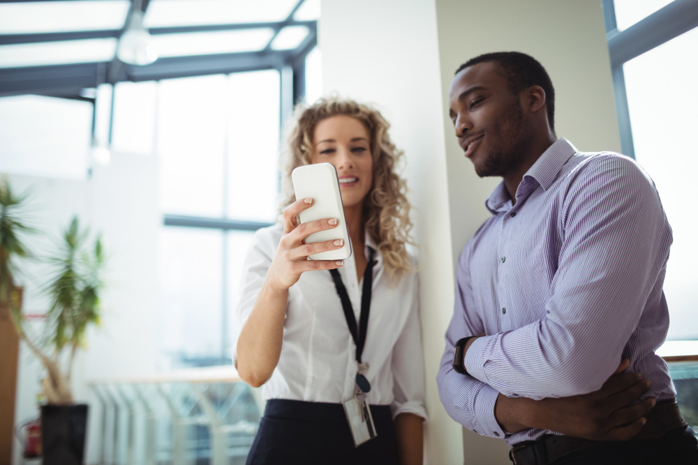 A woman showing her smartphone to a male colleague in a modern office setting.