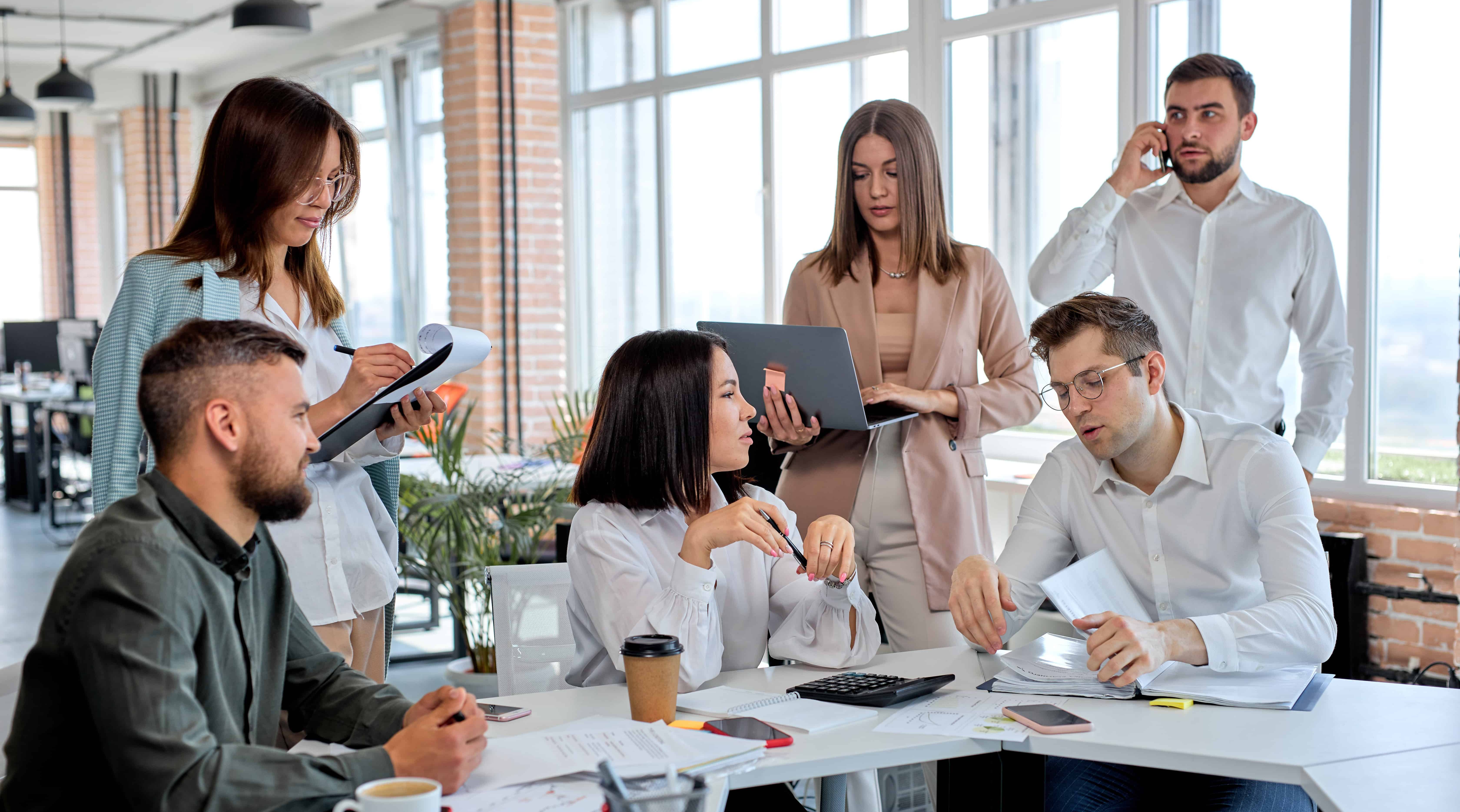 Business people working as team in modern office, discussing business plans and strategies, share ideas. Caucasian men and women in formal wear having talk, communicating, while sitting behind table
