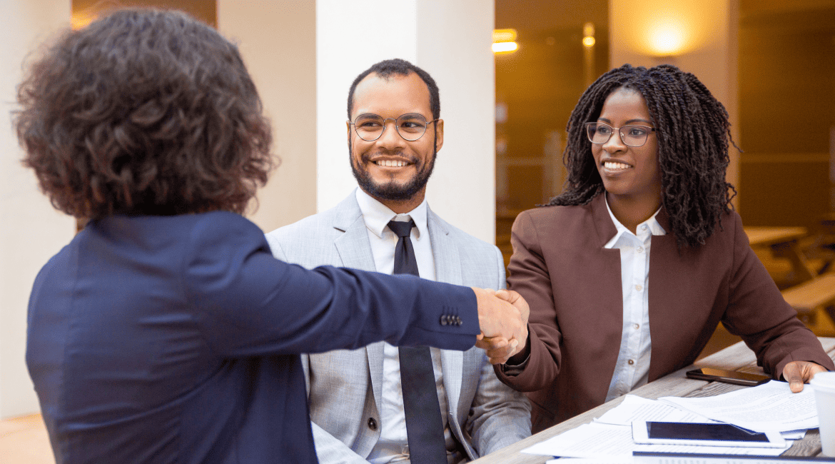 An indivudal shaking hands with another person while the third one is smiling