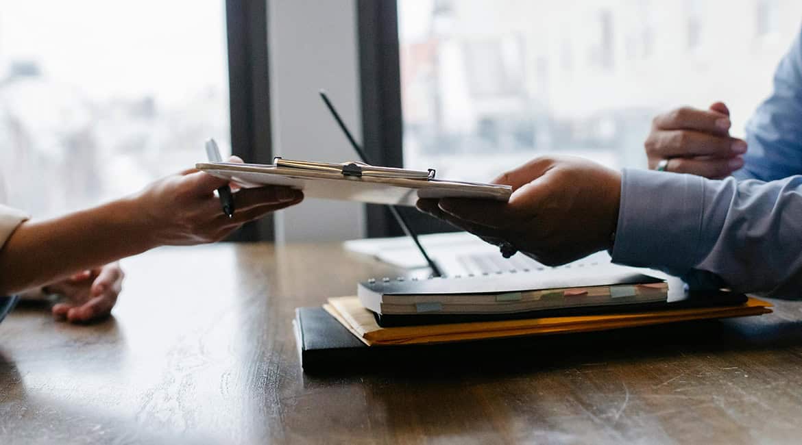 Hands of HR team members in an office holding pens, focusing on compliance-related documents