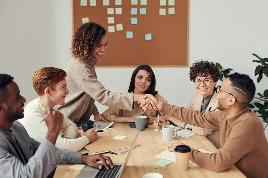 Office team working and discussing their tasks around a conference table, with smiles and engaged expressions, creating a collaborative and positive work atmosphere.
